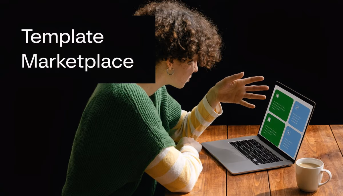 A person with curly hair wearing a green sweater using a laptop at a wooden table.